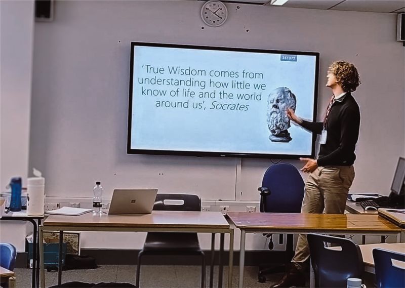 Ethan Green lecturing in a classroom in front of a slide quoting Socrates
